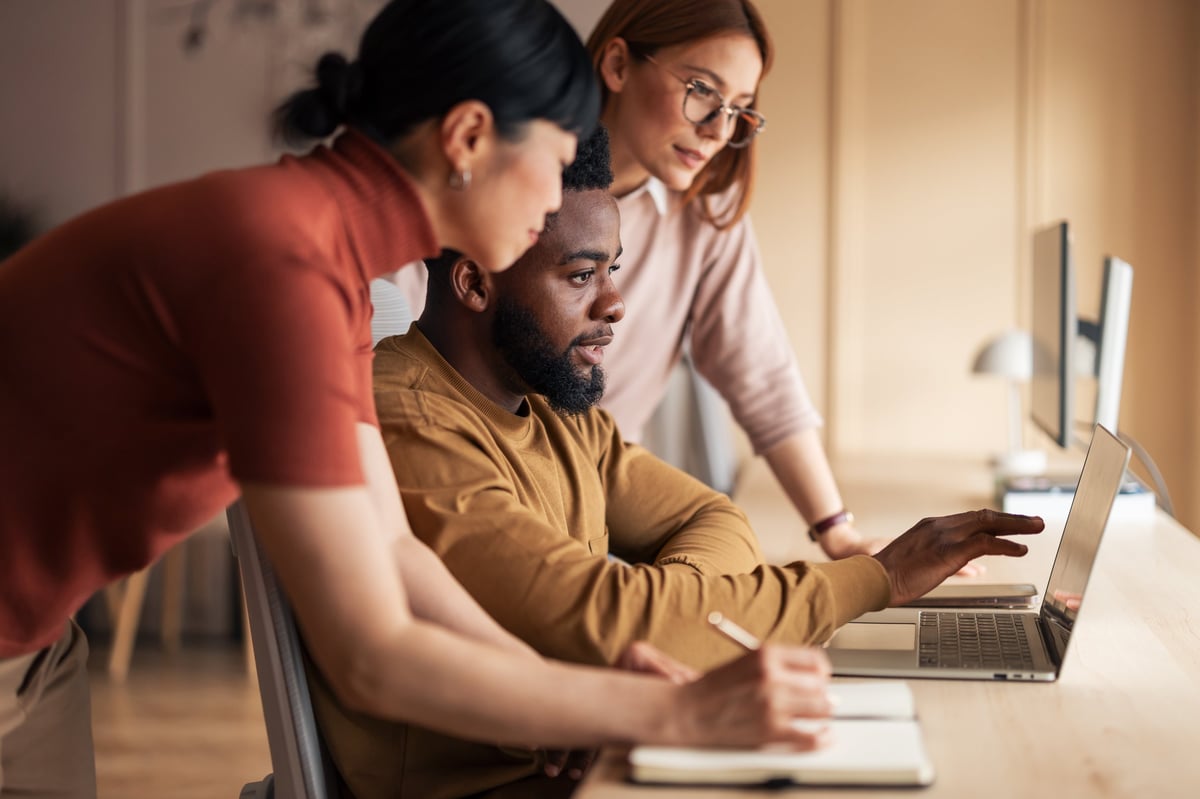 A team of professionals working collaboratively at a desk, utilizing a laptop for a shared project in a modern office